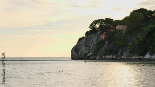 Handheld shot, cam follow the sea bird flying above water surface, koh Phangan island landscape at sunset time photo