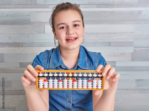 Happy girl in blue blouse holding abacus over light background. Mental arithmetic school. Kids development, skill at mental arithmetic.