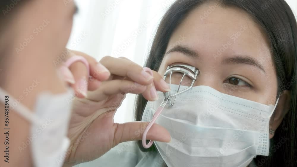 Mirror reflection asian woman wear surgical face mask make eyelash curler for go out to work after unlock Coronavirus lockdown. Reopenning , restart, Self-quarantine and social distancing concept. Mirror reflection asian woman wear surgical face mask make eyelash curler for go out to work after unlock Coronavirus lockdown. Reopenning , restart, Self-quarantine and social distancing concept.