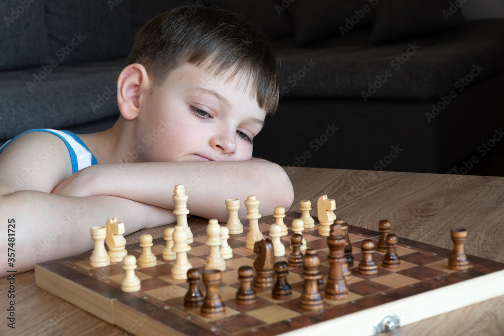 The serious child lost in thought playing chess. Playing board games, on coronavirus quarantine. The child playing chess.