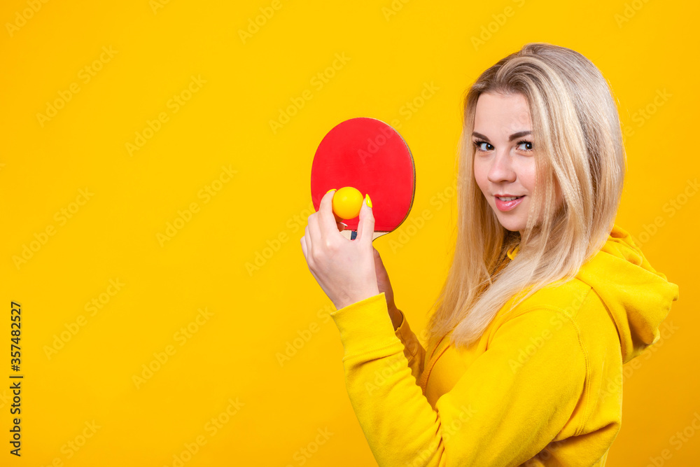 Attractive beautiful young blonde woman in casual yellow sporty clothes play ping pong, holding a ball and racquet. Attractive beautiful young blonde woman in casual yellow sporty clothes play ping pong, holding a ball and racquet.