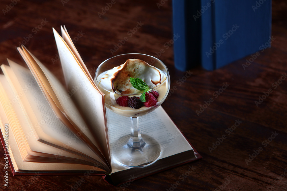 Dessert with berries and cream is on the pages of an open book. The concept of reading and leisure. Copy of the space. Photo in the interior on a dark background. Top view