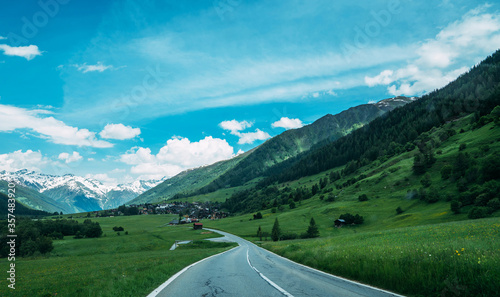 Picturesque road leading towards a snow capped mountains in Swiss Alps in a beautiful summer day. Mountain road. Landscape with green meadows, alpine village and blue sky with clouds. © eskstock