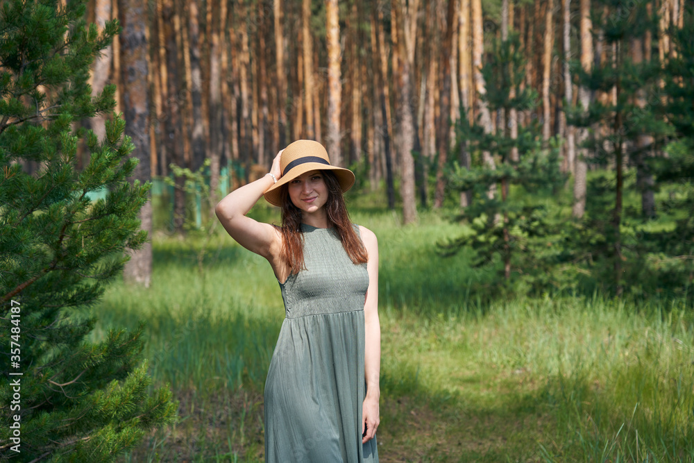 Young woman in a straw hat in a summer forest at the summer day.
