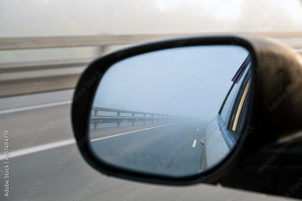 Look in the rear view mirror of a car. Foggy morning.