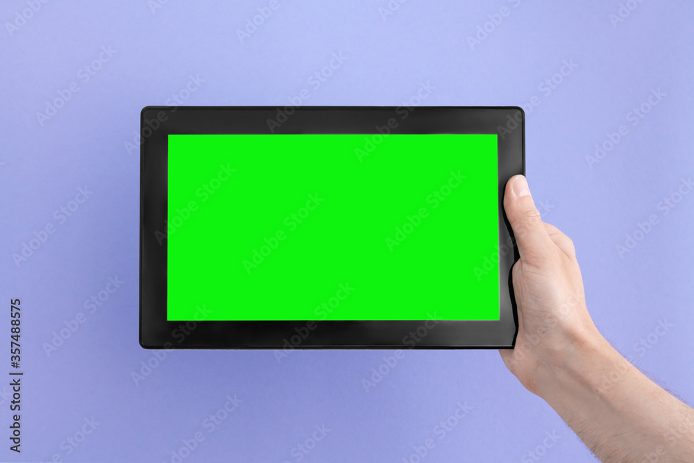 Tablet computer with green screen in man's right hand on an lilac background.