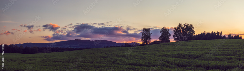 Fototapeta premium panorama landscape at sunset - meadow, trees and hills and clouds illuminated by the setting sun
