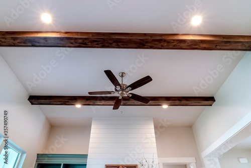 Ceiling fan with lights between decorative wood beams inside living room of home