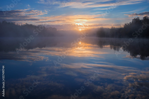 dawn over a foggy lake in the forest early in the morning. Blue sky and sun reflected in water