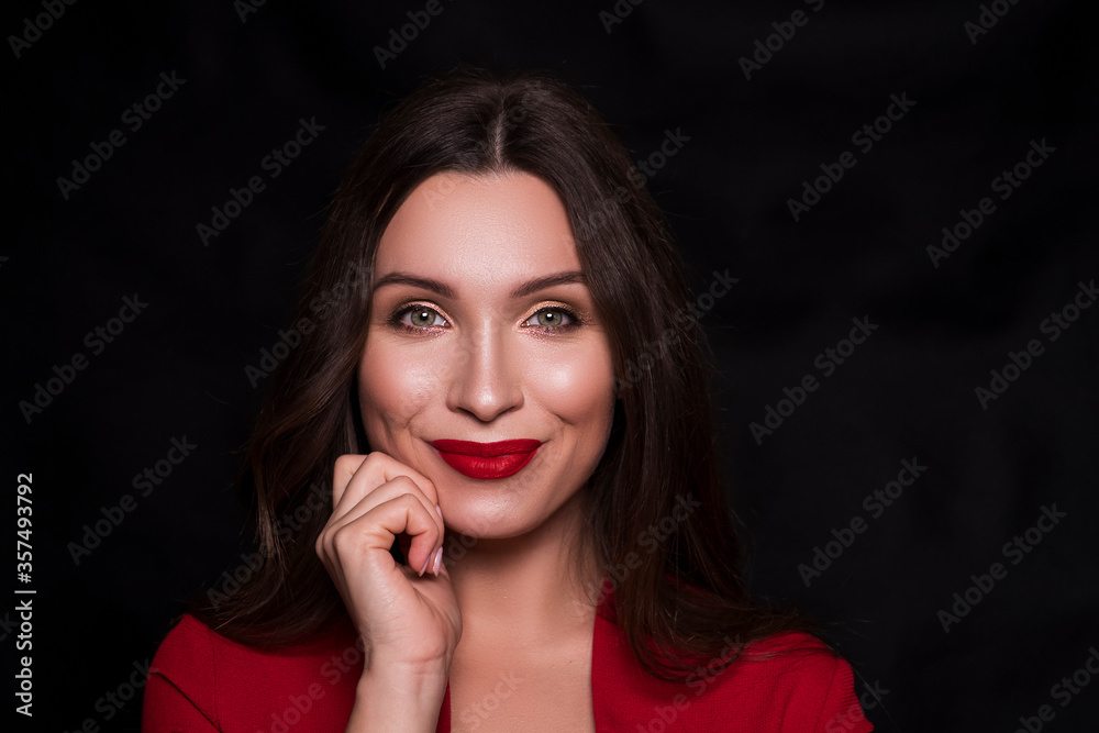 Emotional head shot portrait of a brunette caucasian woman in red dress and with red lips on black background. She look happy, smiling, with hands near her face Emotional head shot portrait of a brunette caucasian woman in red dress and with red lips on black background. She look happy, smiling, with hands near her face