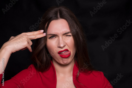 Emotional head shot portrait of a brunette caucasian woman in red dress and with red lips on black background. She make unhappy, dusgusting emotions