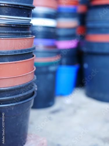 Stack of round multi coloured plastic flower pots with more stacks In background