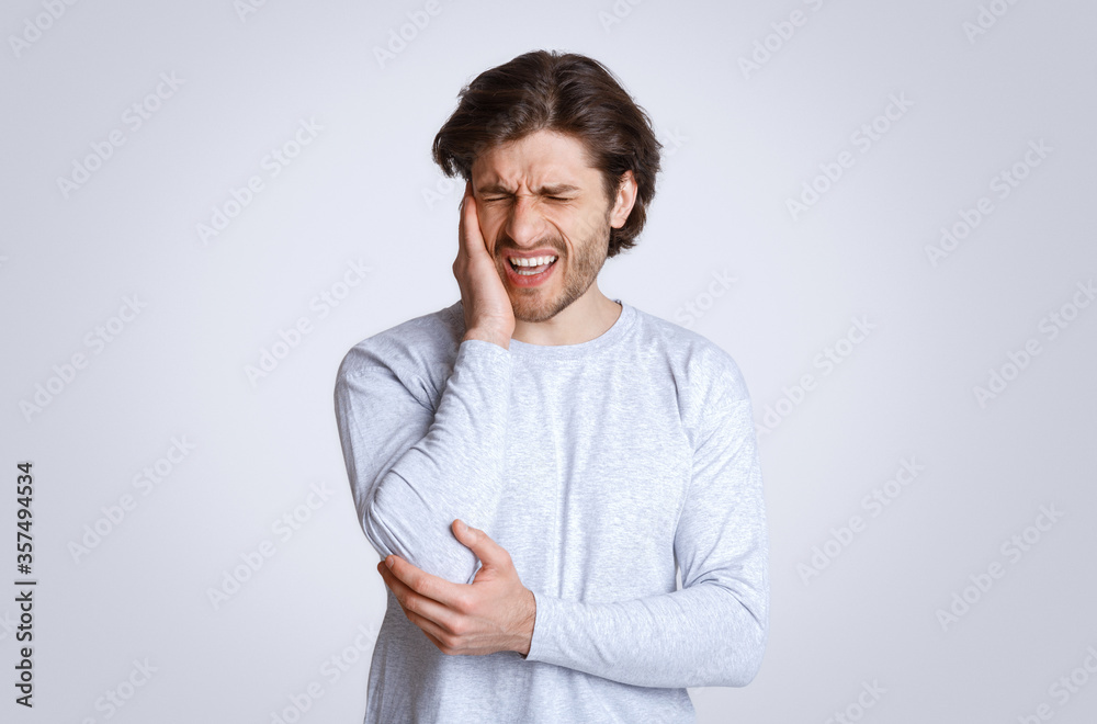 Sharp pain in ears. Man grimaces and holds his hand to sore spot Sharp pain in ears. Man grimaces and holds his hand to sore spot