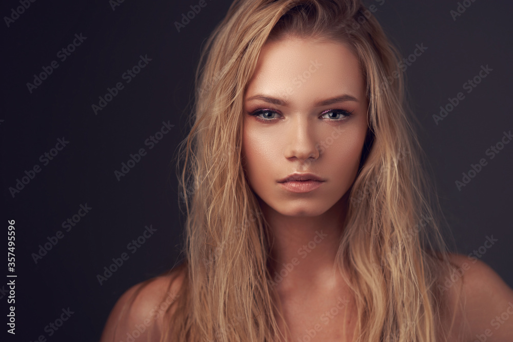 Fototapeta premium Closeup face portrait of young pretty caucasian woman with long blonde woman looking in camera and posing against gray background. Shallow DOF.