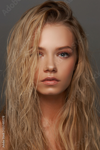 Closeup face fashion beauty portrait of young beautiful caucasian blonde woman with wet hair and makeup posing against gray background.
