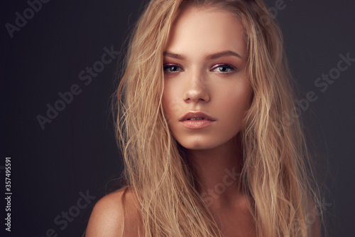 Closeup face portrait of young pretty caucasian woman with long blonde woman looking in camera and posing against gray background. Shallow DOF.