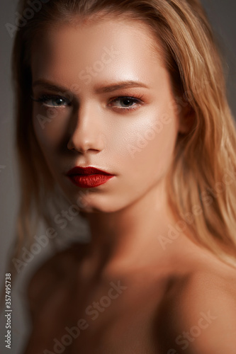 High fashion closeup beauty portrait of young stunning woman with long straight blonde hair, perfect makeup and red lips against gray background