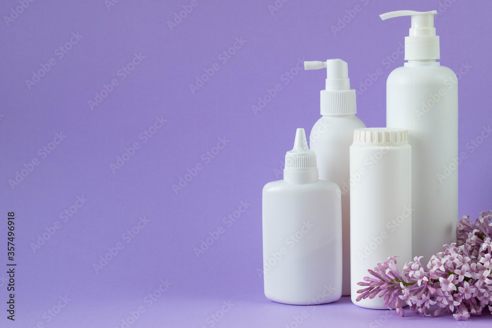 Jar with baby powder, bottle of talcum powder, liquid soap and shower gel isolated on a purple background with a branch of lilac. Jar with baby powder, bottle of talcum powder, liquid soap and shower gel isolated on a purple background with a branch of lilac.