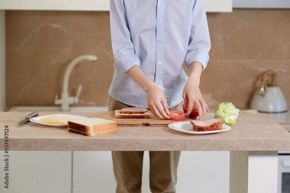 A boy in a blue shirt is preparing a sandwich of vegetables, meat and bread.
