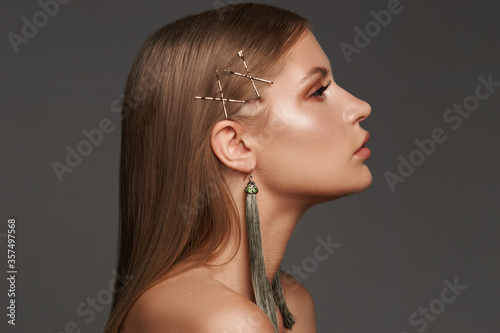 Beautiful young woman with long dark straight hair. Brunette with perfect makeup wearing long green earrings closeup portrait against gray background photo