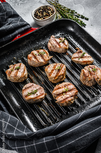 grilled pork tenderloin medallions with fresh herbs in a pan. gray background. Top view