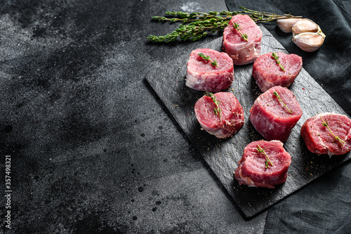 Raw pork medallion steaks with pepper and thyme. black background. Top view. Copy space