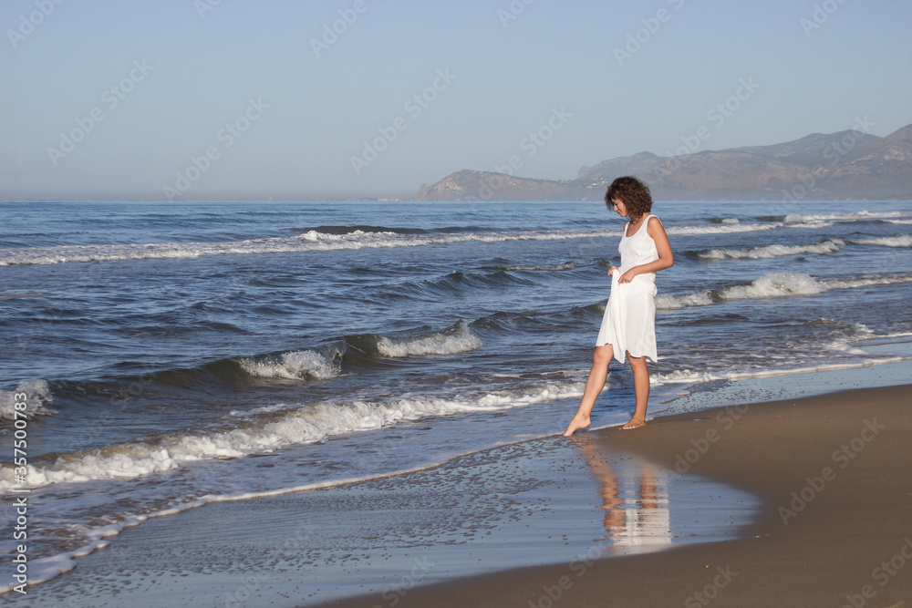 Young woman in white dress walking near a beach in hot sunny summer day, clear sky