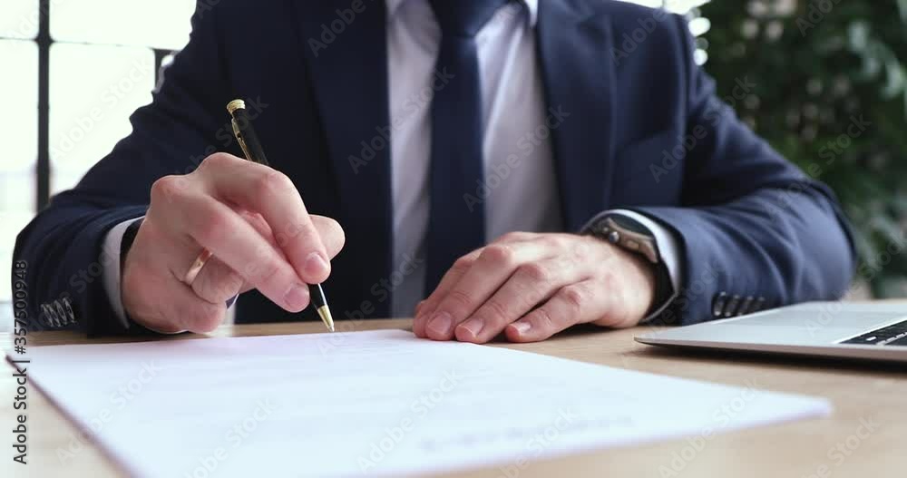 Close up concentrated young businessman in formal wear carefully reading contract terms of conditions, putting signature on paper. Focused executive ceo signing report after checking information.