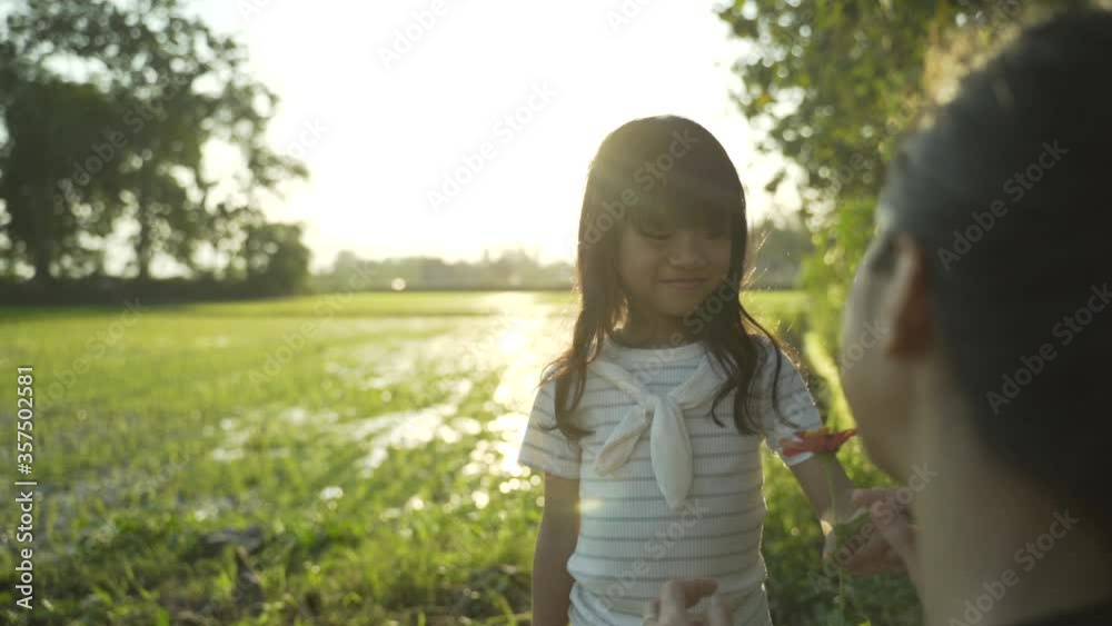 lovely asian daugther giving flower to her mother while playing in the field lovely asian daugther giving flower to her mother while playing in the field