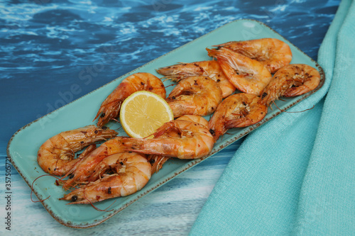 fried shrimps with lemon on a blue plate on a blue sea table and fabric napkin. Banner, menu, poster. Copy space.