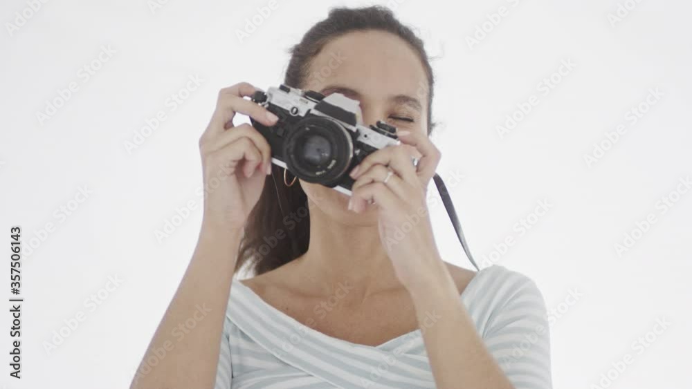 Young attractive dark-haired female dressed in white stripped top points camera objective at viewer and tries to find the best position for picture. 4K footage. Young attractive dark-haired female dressed in white stripped top points camera objective at viewer and tries to find the best position for picture. 4K footage.