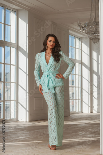 Young beautiful woman with long brown wavy hair in green lace suit standing and posing in luxury interior with french windows on a sunny day. Interior fashion portrait with beautiful light and shadows Free Download Young beautiful woman with long brown wavy hair in green lace suit standing and posing in luxury interior with french windows on a sunny day. Interior fashion portrait with beautiful light and shadows - GFXLoad