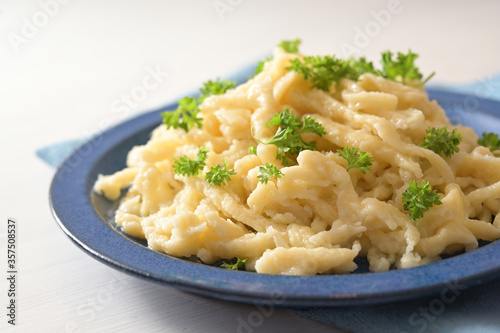 Homemade spaetzle with parsley garnish on a blue plate and a white table, typical dish in Schwaben, southern Germany and Austria, selected focus