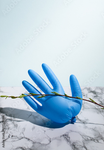 Blue latex glove on marble background with blooming twig