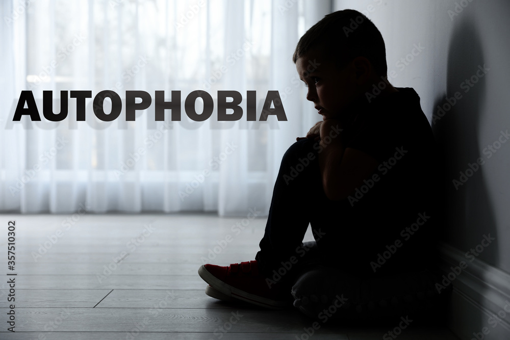Sad little boy sitting alone near light wall at home. Autophobia Sad little boy sitting alone near light wall at home. Autophobia