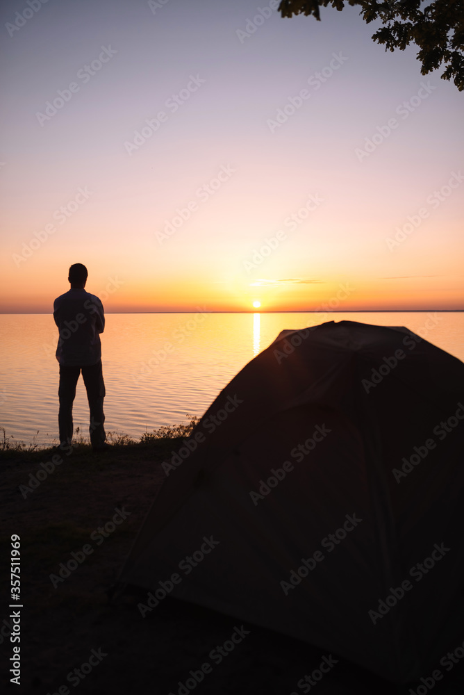 A man meets the sunrise and stands with his back to us