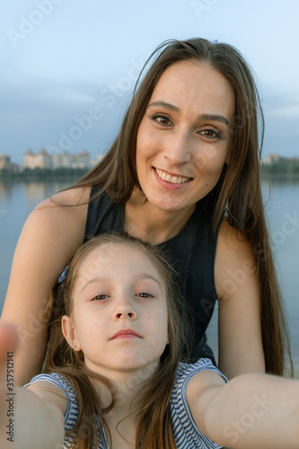 Mom and daughter take selfies and look directly at the camera. They are smile beautifully and seem happy. High quality photo