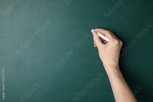 Woman with white chalk near green blackboard, closeup. Space for text