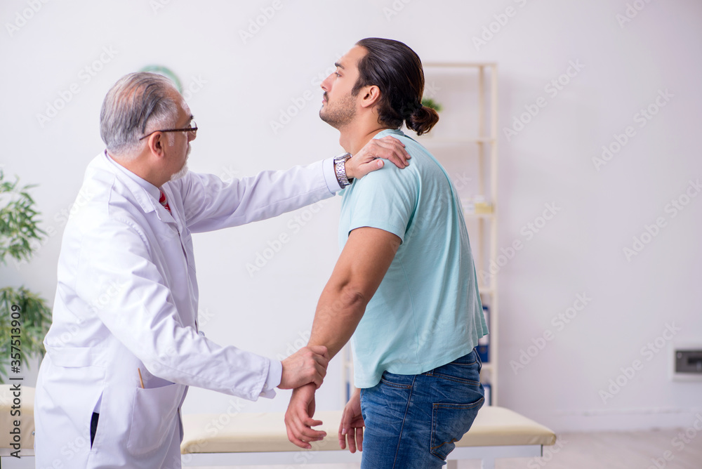 Young back injured man visiting experienced male doctor Young back injured man visiting experienced male doctor