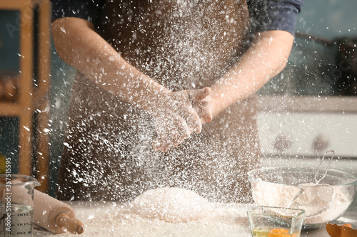 Man sprinkling flour over dough on table in kitchen, closeup