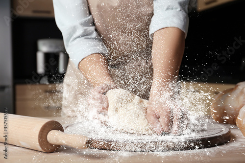 Fotografie, Obraz Young woman kneading dough at table in kitchen, closeup
