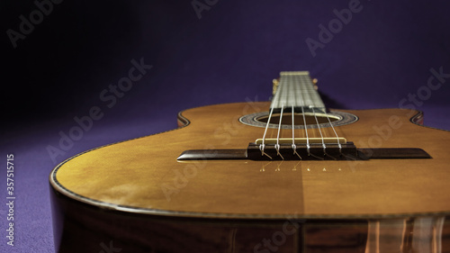 Retrato de una guitarra acústica clásica acostada casi al centro de la imagen, se muestra la caja, el puente, la boca, el mástil y sus cuerdas sobre un fondo oscuro. Sólo la guitarra está iluminada.