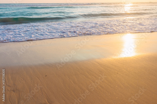 Tropical shore. Seaside background. Sandy beach and soft ocean wave in warm sunset light.