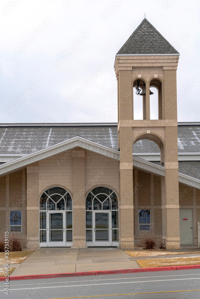 Church facade with glass front doors and modern belfry tower against cloudy sky Church facade with glass front doors and modern belfry tower against cloudy sky