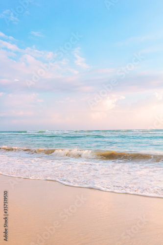 Sandy beach pastel background. Blue cloudy sky and soft ocean wave in warm sunset light