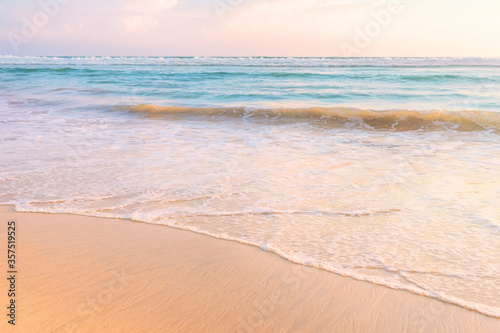Tropical shore. Sandy beach and wavy sea in soft warm sunset light.