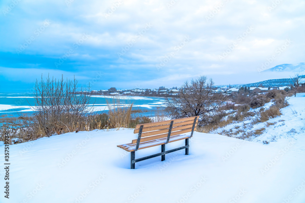 Bench on a snowy terrain with frozen Utah Lake and overcast sky view in winter