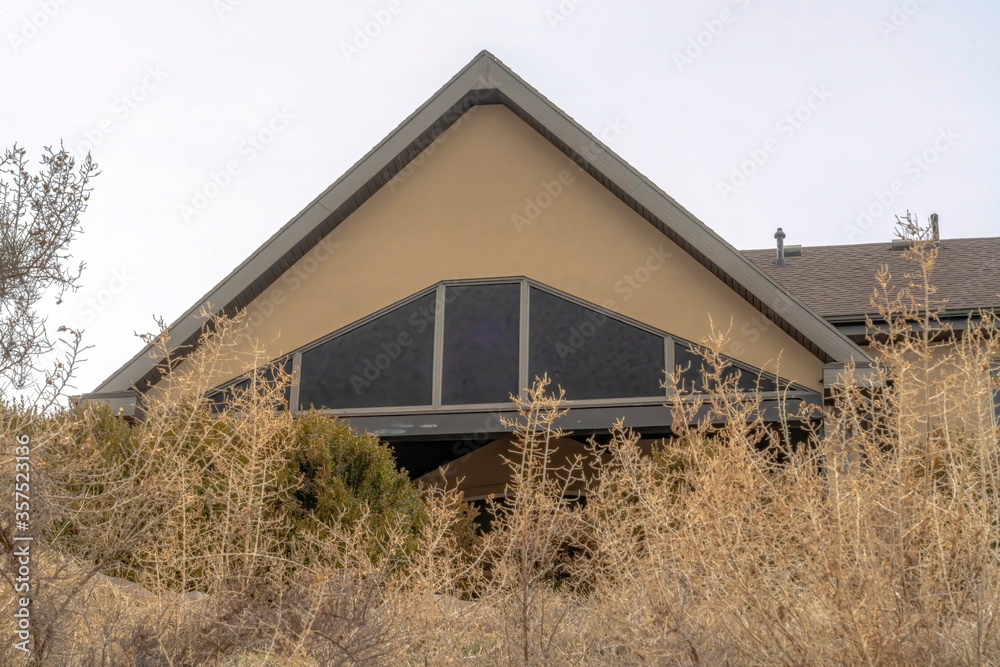 Home exterior with front gable roof at entrance viewed behind grasses and trees Home exterior with front gable roof at entrance viewed behind grasses and trees