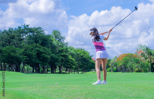 Woman golf player in action being setup address of back swing to hit the golf ball away from T-OFF to the destination on the green, fairway at day light sky.