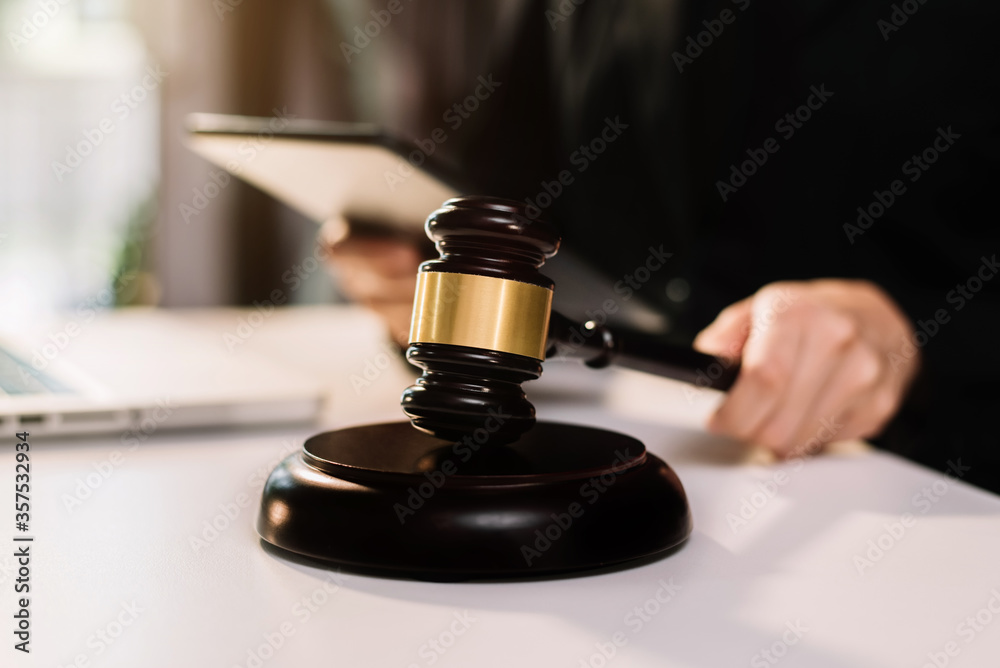 Male judge in a courtroom the gavel, working with digital tablet computer on wood table in sun light. Male judge in a courtroom the gavel, working with digital tablet computer on wood table in sun light.